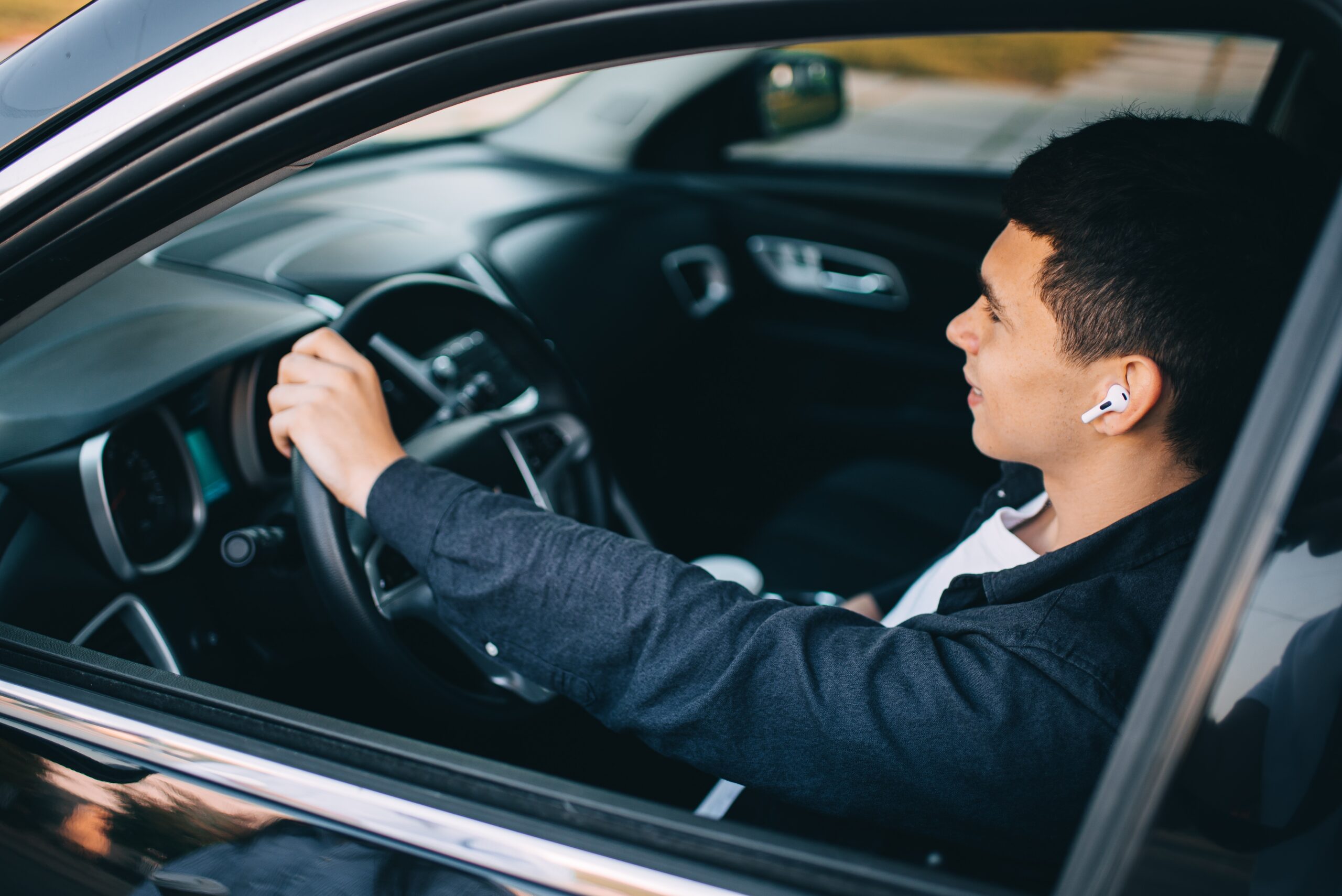 Driver wearing wireless earbuds behind the wheel representing legality of headphones while driving in Texas